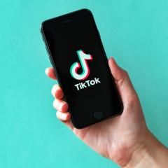 Studio shot of hand holding Apple iPhone 8 with TikTok logotype on a screen.