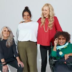 A diverse group of women modelling a clothing line in front of a light grey backdrop.