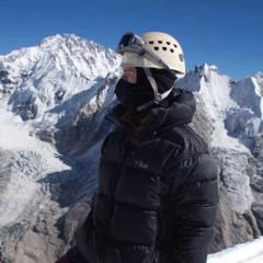 An image of UQ student Emerald Gaydon standing in front of snow-covered mountains and a clear blue sky during her summit of Tsorku Peak in the Himalayas.