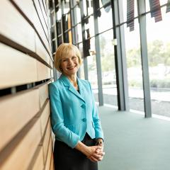 Professor Deborah Terry leaning on a wooden panelled wall and smiling