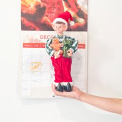 A Christmas elf in front of a calendar showing the month of December
