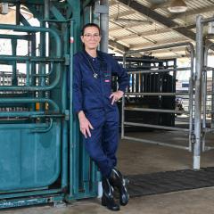 An image of first-year Bachelor of Veterinary Technology student Yasmine Gray, wearing overalls and gumboots, standing next to a cattle crush at UQ's Gatton campus.