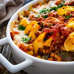 Bowl of noodle casserole with minced meat, mozzarella cheese and vegetables on wooden table