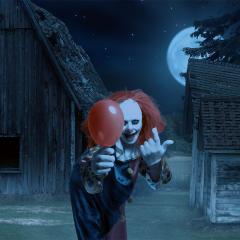 eerie clown with a balloon in hand in front of a scary scene.