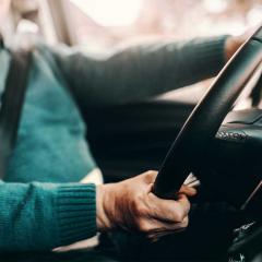 An image of an elderly man's hands holding the steering wheel.