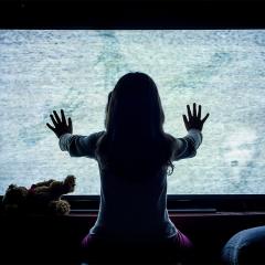 A young girl putting her hands on a fuzzy television screen, reminiscent of a famous scene from 'Poltergeist'.