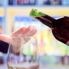 Woman hand rejecting more alcohol from wine bottle in bar.