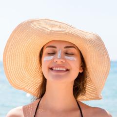 Young woman in hat applying sunscreen under her eyes and on her nose.