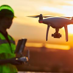 A drone pilot flying a drone on a construction site at sunset.