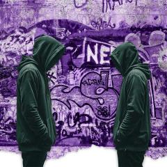 An image of two youths in black hooded jumpers standing in front of a wall covered in graffiti.