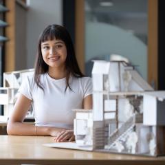 A young smiling woman sitting behind a model of a house