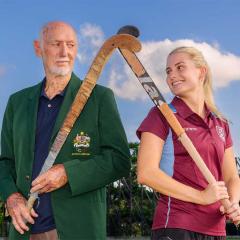 An image of UQ Hockey Club legend and dual Olympian Don McWatters and UQ Division 1 women's captain Morgan Gallagher back-to-back on the UQ hockey playing fields at UQ's St Lucia campus.