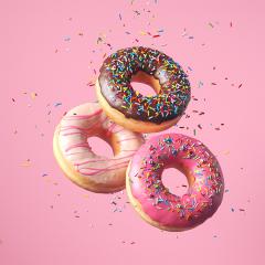 A flat lay image of doughnuts with coloured glaze icing on a pink background