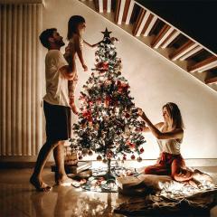 A family decorating a Christmas tree. The daad is lifting his daughter so she can place the star on top of the tree.