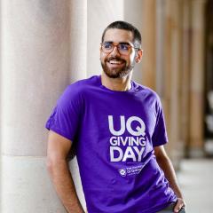 An image of Jackson Daylight wearing a purple UQ Giving Day t-shirt and standing in UQ's Great Court.