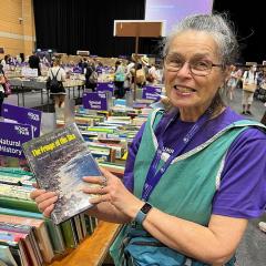Myriam Preker at the book fair, holding a book called "The Fring of the Sea" by Isobel Bennett