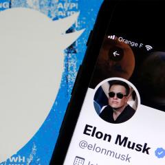 An illustration of the Elon Musk’s Twitter account displayed on the screen of an iPhone in front of the homepage of the Twitter website. 