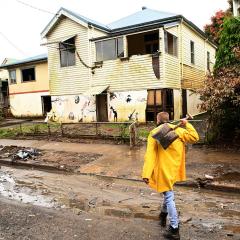 A man walks through mud holding a shovel along a street of flood-damaged homes in Lismore.