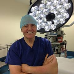 Image of a man wearing scrubs and there is a surgical light set-up behind him