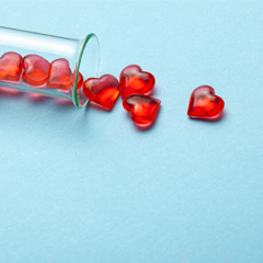 Image of small red glass hearts spilling out of a test tube ont a light blue surface