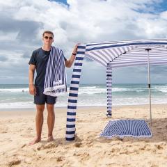 An image of UQ graduate Angus Fraser standing on the beach with a CoolCabanas shade shelter.