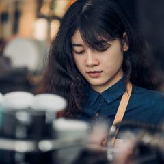 An image of a young woman making coffee in a cafe.