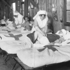 Black and white image shows nurses tending to a row of injured ANZACs in a makeshift treatment ward during WWI.