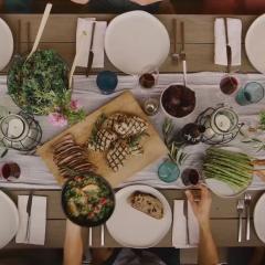 Overhead image of stylishly set dinner table with bowls of salad, roast meats and drinks.