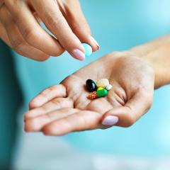 A pair of hands holding vitamin tablets and capsules