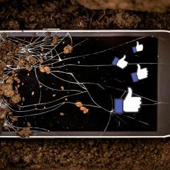 Broken phone in the grave with thumbs-up like symbols floating out of it.