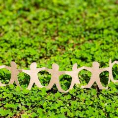 A paper cut out of people holding hands in a line. The paper cut outs are sitting on some moss.