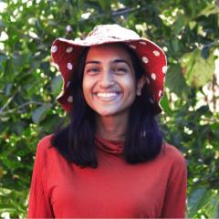 A woman smiles towards the camera wearing a red shirt and a red polka-dot hat.