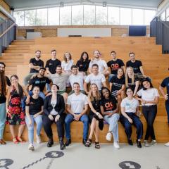 A large group of diverse people smiling towards the camera while sitting on tiered stadium seating.