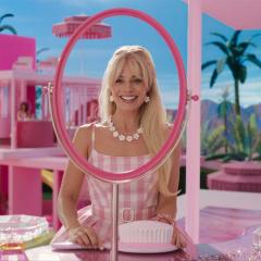 Margot Robbie as Barbie wearing pink and looking through a pink framed mirror