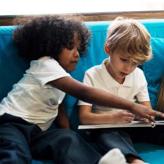 Young school children sitting and reading together on a couch at after school care.