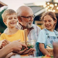 A grandfather sitting with grandchildren on his lap at a family barbecue.