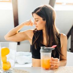 Woman at home drinking orange-flavoured drink, flexing her muscles.