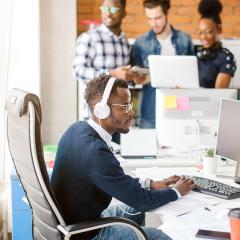 Office worker typing at his desk while wearing headphones because of the noisy room.