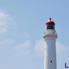 Image of an old white lighthouse with a red top against a blue sky