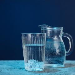 Image of a glass of water and a glass water jug on a bench with a dark blue background