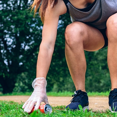 Image of a woman with gloves and running shoes bending down to pick up litter.