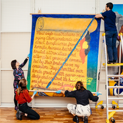 Image credit: Registrars carefully hang Gordon Hookey's "Dundalli Banner" (2021) in the Alumni Friends of UQ Collection Study Room Photo: Josef Ruckli.