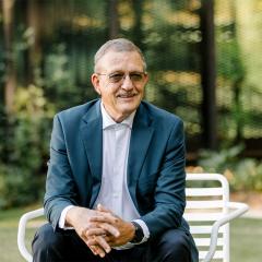 Bob Christiansen sitting on a chair smiling with hands crossed together in front of him.