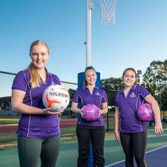 An image of UQ Firebirds Scholarship recipients Savanna Detlefson, Brooke Warburton, and Alyssa Hanson holding netbals at the netball courts at UQ's St Lucia campus.