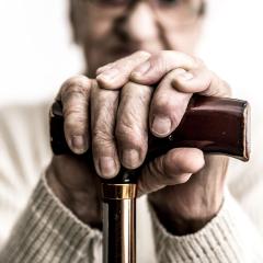 An image of an old ladies hands clasping a walking stick. The image contains a headline, which says, 'a broken system'.