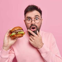 Shocked bearded adult man holds hamburger 