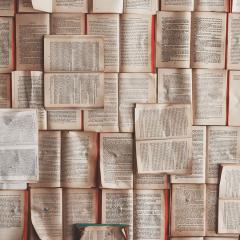 Old books laid out on top of each other with the pages open to create a carpet of mismatched pages.