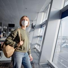 An image of a young woman with a backpack and wearing a face mask while waiting for her plane at an airport.